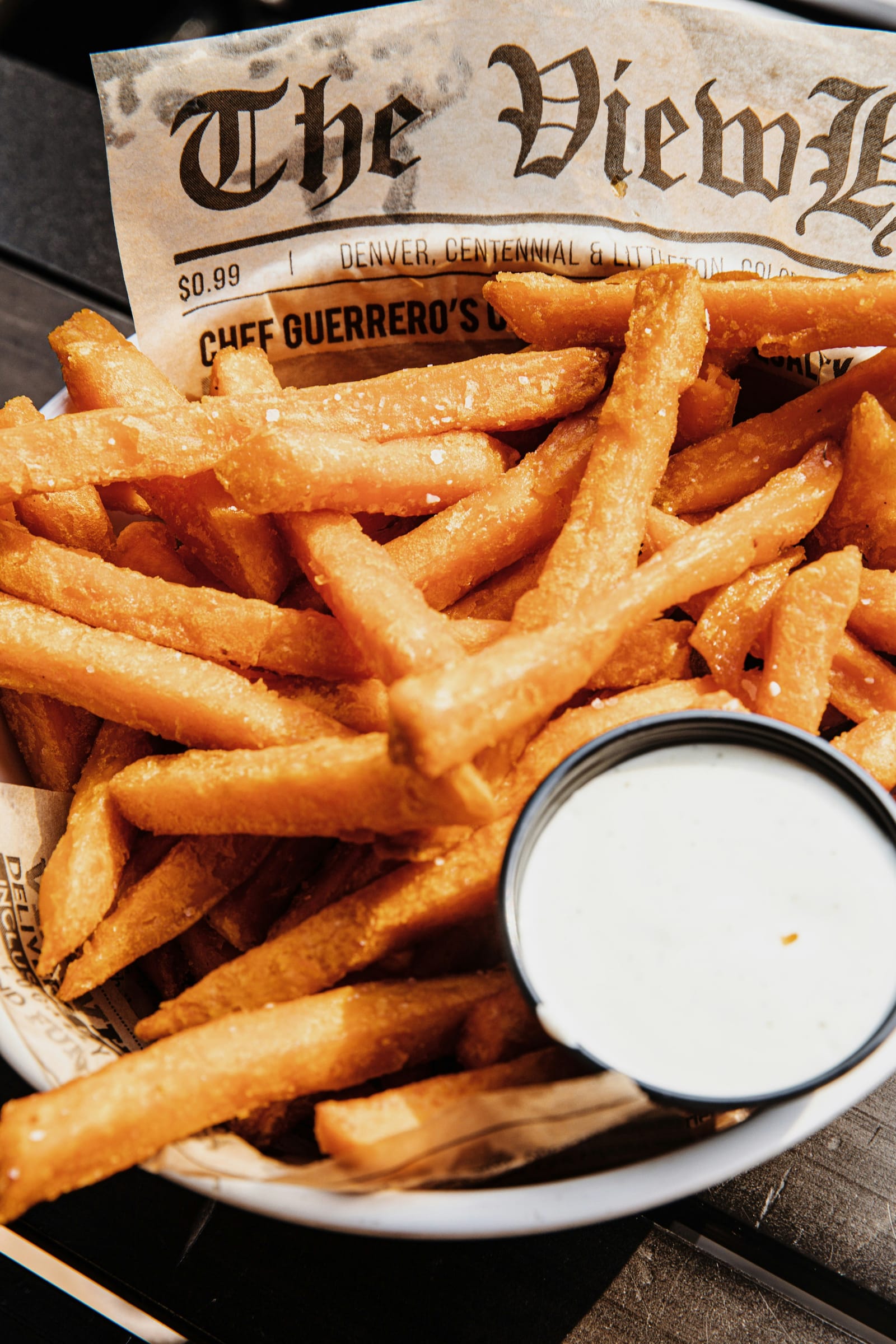 A bowl of golden chips served on printed paper with a small pot of dipping sauce